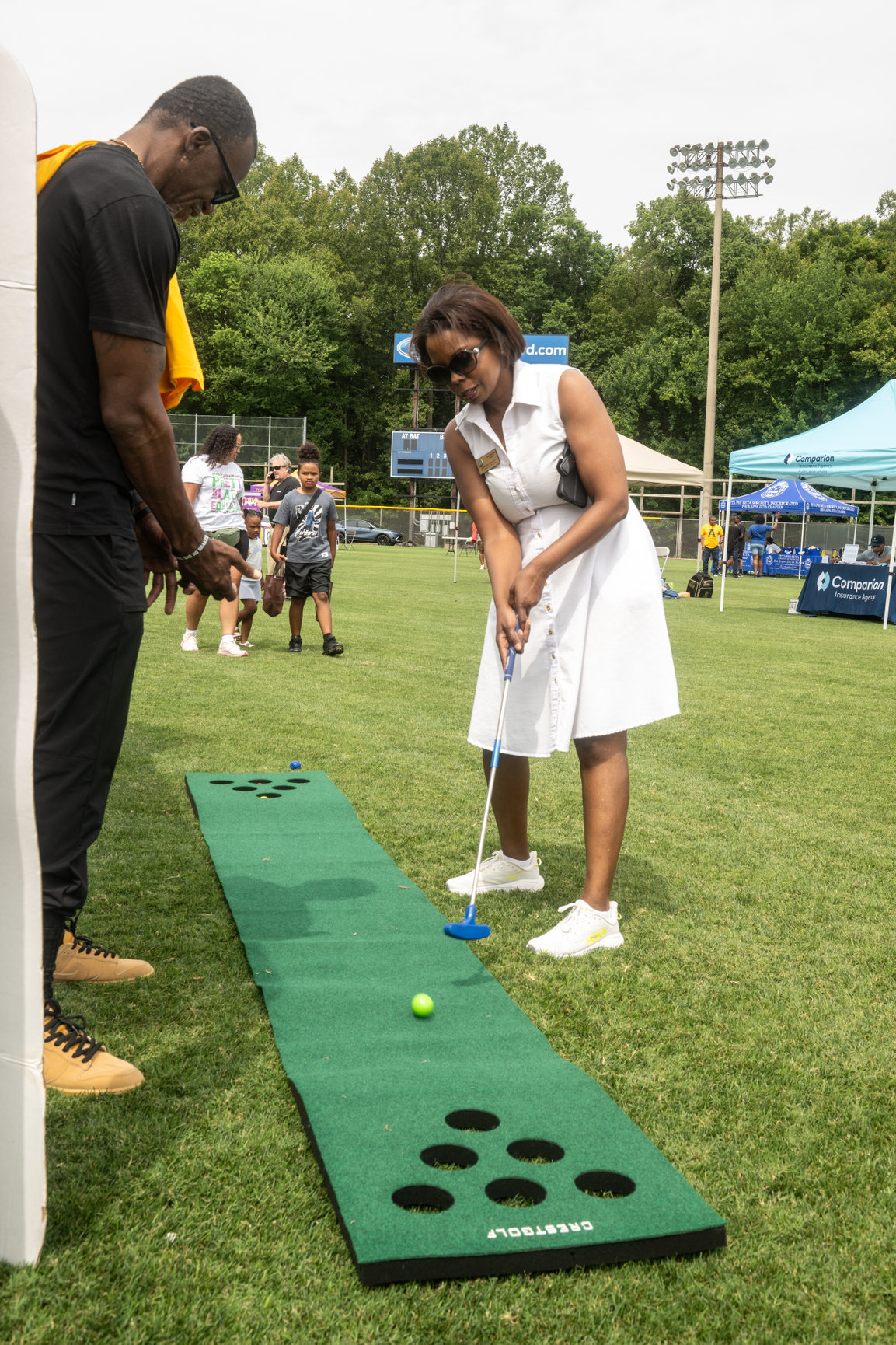 Resident participating in a partner-hosted lawn putting activation beside sponsor tents